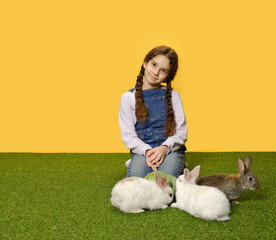 Little schoolgirl is lying down playing with the bunnies in the studio, yellow background. Copy space.