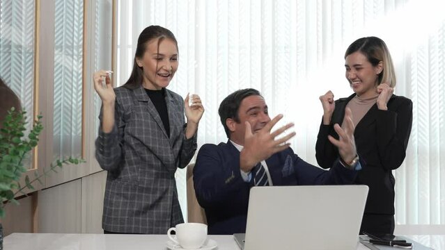 Businessman smile glad to recieve a good news from computer laptop while sitting at a desk in a office, Excited of colleagues raise their hands to celebrate success, business achieves goals.