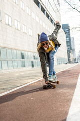 Young woman on longboard riding on a cycle lane, street style dress code