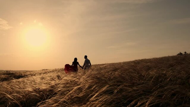 Silhouette of couple in golden field and beautiful sunset. Young and romantic family enjoying. Man hold woman in arms with love on summer evening. People talking and hugging by heart. Two person.
