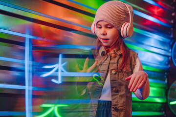 Obraz premium Little girl wearing headphones using smartphone on the colorful neon