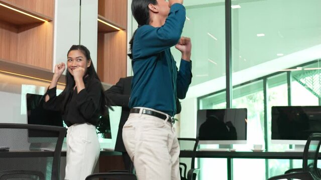 Happy businessman standing up from office desk and start dancing together, business team dancing celebrating success in office, co-workers having fun together enjoy victory dance in modern office.