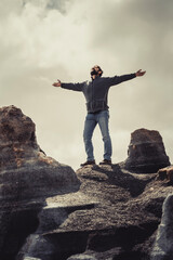 Obraz premium Man standing with arms outstretched against a cloudy grey background on old scenic stones. Concept of freedom and travel destination holiday. People enjoying life. Happiness and success life image