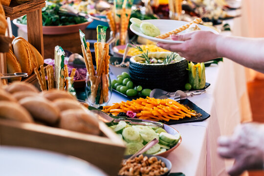 Close up of catering service table full of food and people serving and taking on dishes. Concept of holiday event like wedding or anniversary. Restaurant self service and buffet with delicious