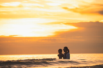 Happy family resting at beach in summer, Mother and baby boy feet at the sea foam at the sunlight water is moving