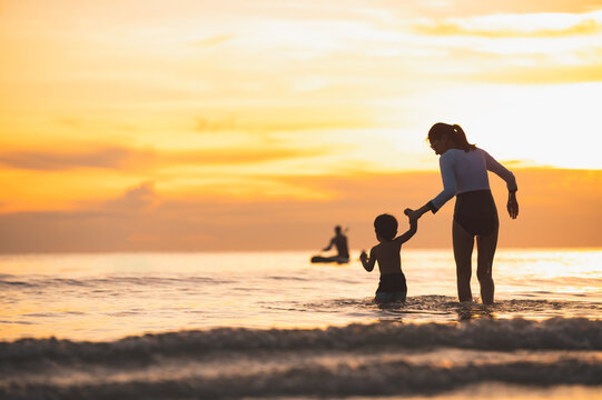 Happy Family Resting At Beach In Summer, Mother And Baby Boy Feet At The Sea Foam At The Sunlight Water Is Moving