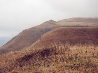 Hills covered with autumn dried grass and fog descending on a cloudy day
