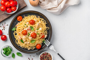 Pasta with baked feta, cherry tomatoes and garlic on a light gray background.