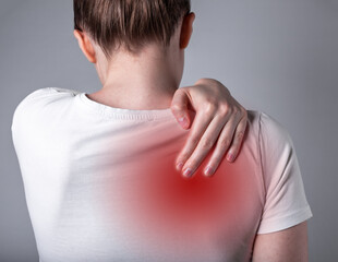 Woman suffering from shoulder blade pain. Trigger point. Hand holding shoulder with red spot...