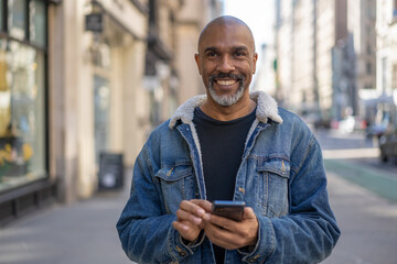 Mature black man in city using cell phone walking on a street