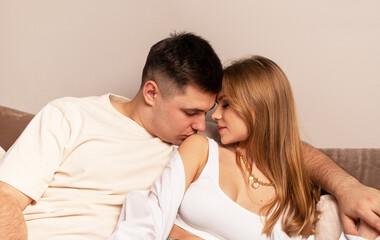 Fototapeta premium Couple sitting on couch. Handsome man kissing wife or girlfriend on shoulder. Passion, love, intimacy concept. Home date. High quality photo