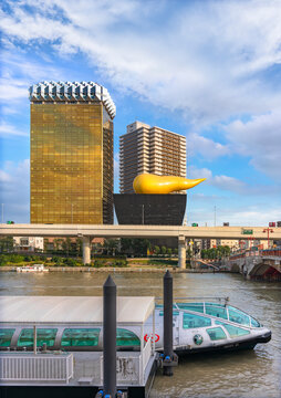 tokyo, japan - october 28 2021: The golden flame sculpture of Asahi Beer Headquarter Building designed by Starck and a water bus designed by manga artist Reiji Matsumoto moored at pontoon of Asakusa.