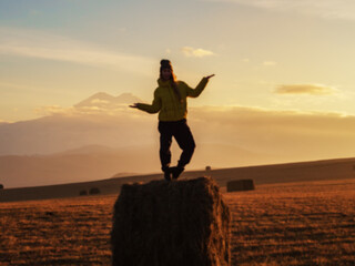 Defocused photo of a woman standing in a pose on a haystack in a wide field against the backdrop of...