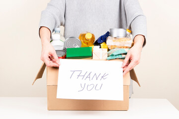 Woman hands holding cardbox with grocery products and card with inscription Thank you. Volunteer...