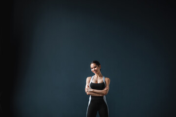 Fototapeta na wymiar Happy young woman in sportswear smiling. Muscular fitness model on dark background