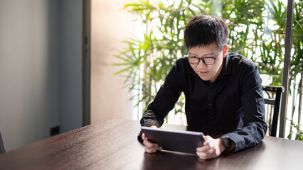 Young Asian businessman using digital tablet in office meeting room. Male entrepreneur reading news on social media app. Online marketing and Big data technology for E-commerce business. 