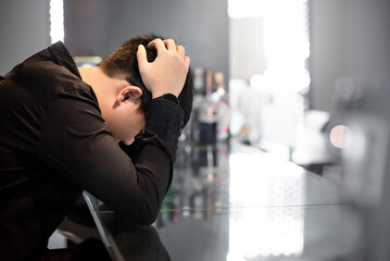 Asian man in black shirt feeling headache and hangover at bar counter in the pub. Mental health...