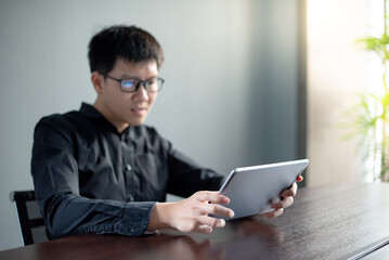 Young Asian businessman using digital tablet in office meeting room. Male entrepreneur reading news on social media app. Online marketing and Big data technology for E-commerce business. 