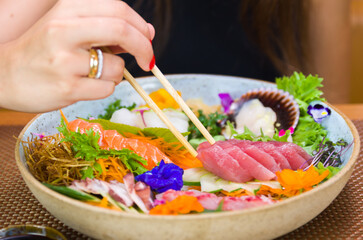 Woman eating delicious sashimi, closeup on chopsticks.