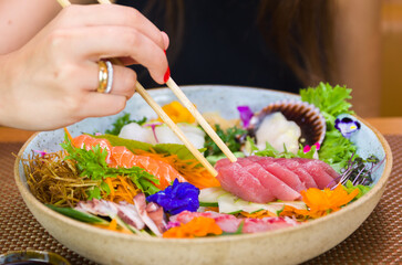 Woman eating delicious sashimi, closeup on chopsticks.