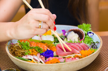 Woman eating delicious sashimi, closeup on chopsticks.