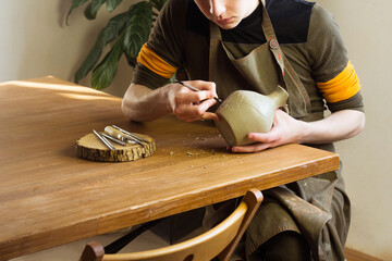 Potter carving ornament on jug. Master working in Pottery studio with equipment Wooden Modeling Tools set