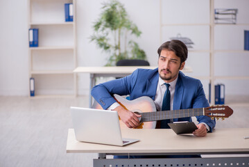 Young male employee playing guitar at workplace