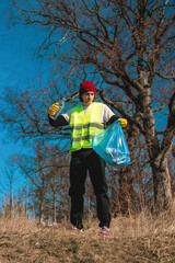 Man nature activist in yellow vest puts plastic bottle in the blue trash bag outdoors