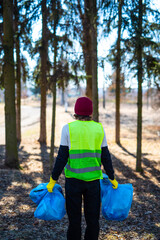 Male nature activist in yellow vest and gloves stands with holding blue trash bags back photo