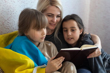 mother and two daughters are reading with the flag of ukraine in bed