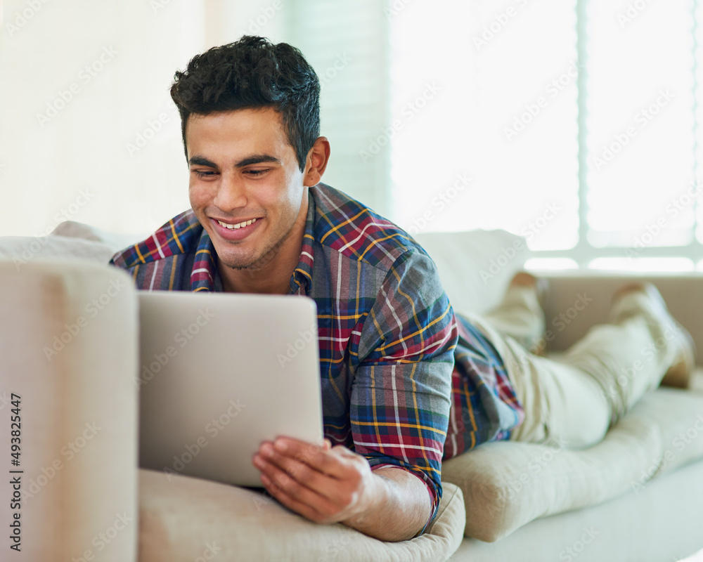 Poster hes hooked on social media. shot of a handsome young man using his laptop while relaxing on the sofa