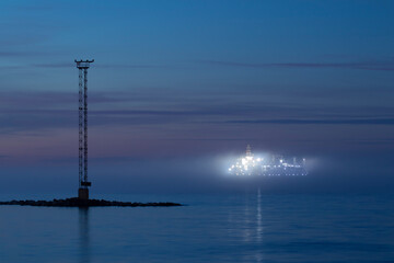 A big illuminated ship navigating in thick fog  near an island in the night after sunset with copy space