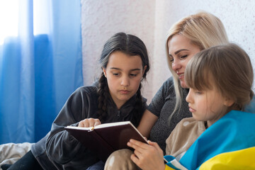 mother and two daughters are reading with the flag of ukraine in bed