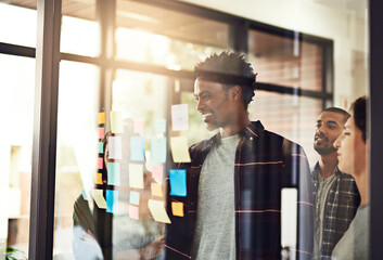 It all starts with an idea. Cropped shot of coworkers using sticky notes on a glass wall during an...