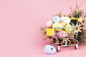 Colorful easter quail eggs in shopping cart on pink background. Copy space. Minimal Easter concept.