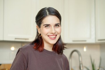 Portrait of young happy smiling brunette woman in cozy home kitchen