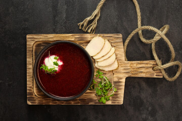 Fototapeta na wymiar Traditional Ukrainian russian borscht red soup in black plate on wood board on a dark background. Borsch with meat, sour cream and greens. Banner, copy space.