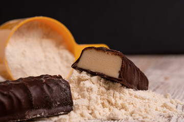 a sweet bar made of whey protein next to a scoop of protein powder for sports nutrition.