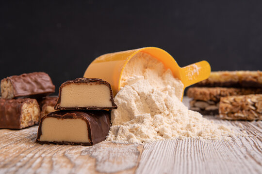 a sweet bar made of whey protein next to a scoop of protein powder for sports nutrition.