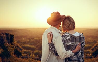 Young couple watching sunset hugging together in nature during summer hike