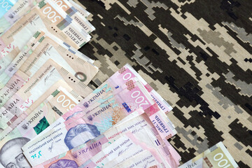 Ukrainian hryvnya bills on fabric with texture of Ukrainian military pixeled camouflage. Cloth with...