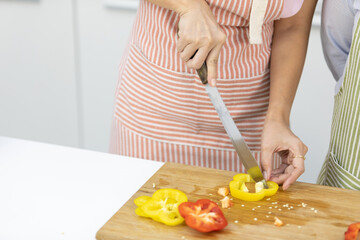 close up woman hands cutting fresh chili peppers on wooden cutting board