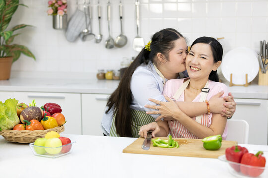 young teenage girl with down syndrome hugging and kissing her mother while cooking food in the kitchen