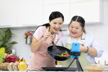 mother and down syndrome teenage girl or her daughter cooking food together and live streaming...