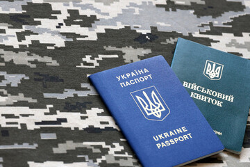 Ukrainian military ID and foreign passport on fabric with texture of pixeled camouflage. Cloth with...