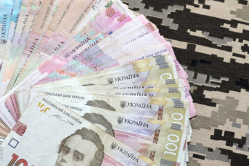 Ukrainian hryvnya bills on fabric with texture of Ukrainian military pixeled camouflage. Cloth with...