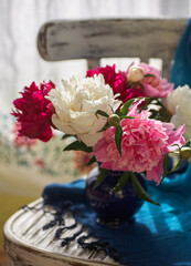 Still life with white and pink peonies in a blue vase on vintaje chair