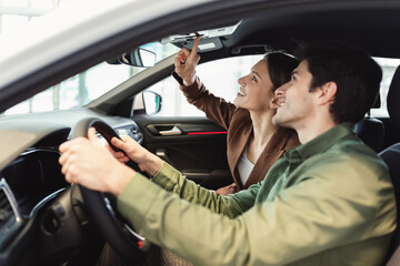 Happy millennial couple test driving new car at automobile dealership