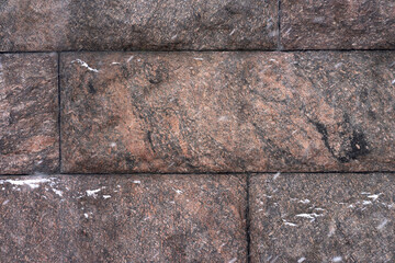 A red granite wall in the snow. Granite background. Photo of granite stone texture.