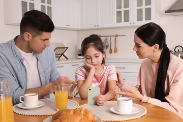 Internet addiction. Parents scolding their daughter while she using smartphone at table in kitchen